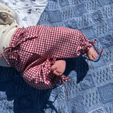 Baby lying on a blue textured blanket wearing a red/white gingham pants.